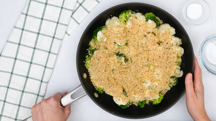 Frying pan with cauliflower and broccoli topped with Alfredo sauce and bread crumbs close up in woman hands. Step by step vegetable casserole recipe, cooking process
