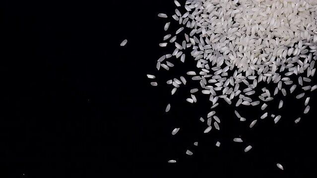 Pouring long raw rice on a black, dark background from above. White rice is slowly spilling on the dark table. Slow motion video
