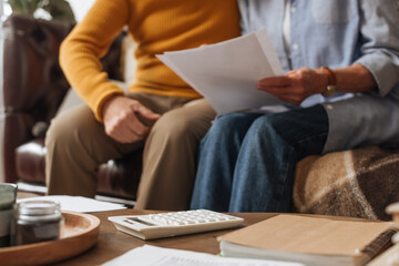 cropped view of elderly couple with bills sitting near white calculator on table on blurred background at home