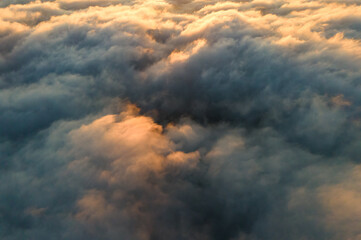 Aerial view over surface of white dense clouds at sunset.