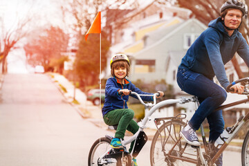 Portrait of a little boy ride on a tow tandem bike with flag attached to father on urban street