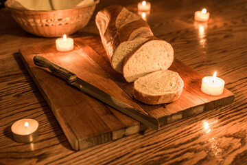 Loaf of bread on a wooden cutting board background. Slicing traditional homemade bread on wood grain table. Candle lights on a table and bread knife