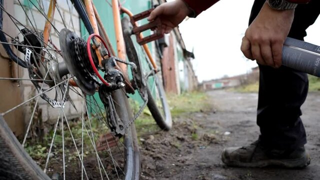 The guy uses the clean liquid from a spray can to clean the bike chain from dirt.