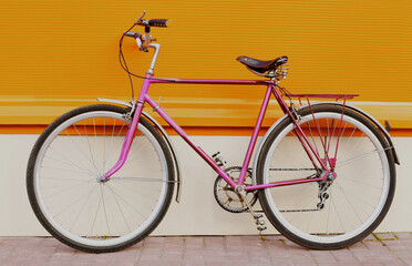 Retro pink bicycle standing in the city on an orange background