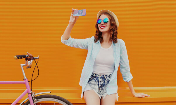 Happy young smiling woman taking selfie picture by smartphone with bicycle on an orange background