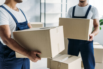 cropped view of multiethnic movers in uniform carrying boxes in apartment