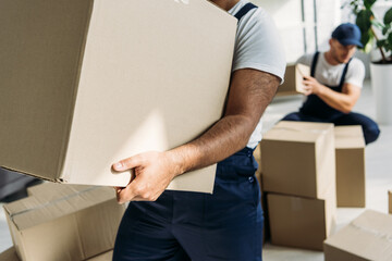 cropped view of indian mover holding carton box near coworker on blurred background