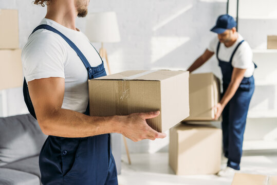 cropped view of mover holding box near indian coworker on blurred background