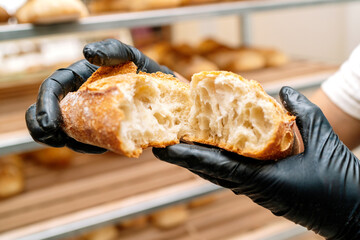 selective focus of han of baker showing how to cut the crumb from a loaf of wheat bread with his hands and protected by black gloves