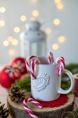 Tazza bianca con bastoncini di caramelle su tavolo di legno dove sono sparse decorazioni natalizie 