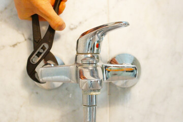 A close up of a hand holding a plumbing spanner screwing a fitting on wash basin waste pipe. 