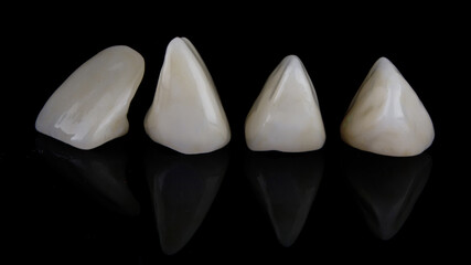composition of four ceramic dental veneers on a black background with creative reflections