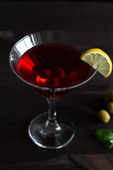 cosmopolitan cocktail in the bar. martini glass of red cocktail with olives and lemon with green mint on wooden background. Glasses for martini on the black table. copy space. alcohol drinks. vertical
