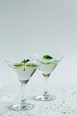 cocktail in the bar. two martini glasses of cocktail with green mint on white background. alcohol drinks. Glasses for cocktail with lemon on the table. copy space. vertical