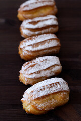 French eclairs on table. vanilla eclairs or profiteroles on a wooden table. Traditional french tasty dessert on dark background. copy space. vertical
