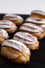 vanilla eclairs or profiteroles on a wooden table. Traditional french tasty dessert on dark background. copy space. vertical