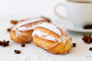 Close-up vanilla eclairs on a plate on background. Coffee cup with coffee beans and anise star, cinnamon sticks on white table. copy space. Traditional french tasty dessert.