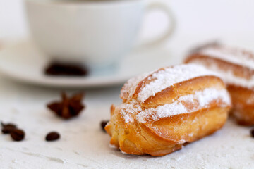 Close-up vanilla eclair on a plate on white background. Coffee cup with coffee beans and anise star, cinnamon sticks on white table. copy space. Traditional french tasty dessert.
