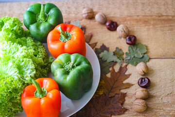 Bell peppers and lettuce leaves are on a plate. Around on a wooden background are yellowed oak leaves and walnuts in shell