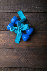 two blue dumbbell with a gift bow and blank paper tag, heart on wooden planks, sport holiday concept