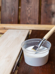 Selective focus. A container with paint and a brush. The horizontal boards are painted with white paint and a brush. Renovation and design. Place for your text. Copy space.