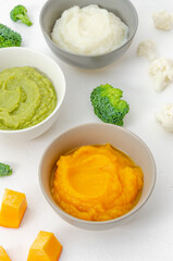 Baby food. Variation of the three homemade vegetable puree in bowls. Pumpkin puree, cauliflower puree and broccoli puree on a white background. Top view.
