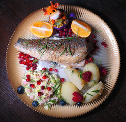 Roasted fish plate with lemon, pomegranate grains and traditional Russian olivie salad