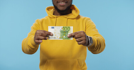 Close up of happy African American man holding in hands euro banknotes isolated over blue background. Euro Money. Euro cash background.