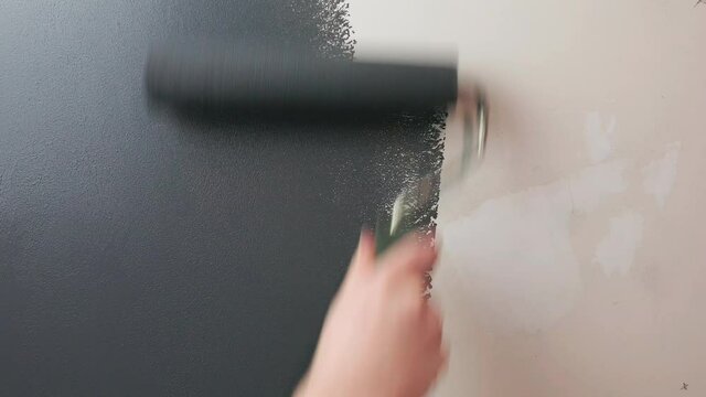 Roller paints the wall with gray paint. Craftsman applies gray paint to the wall using a roller.