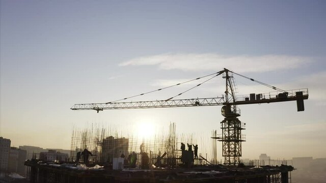 Panoramic aerial view of balks and builders silhouettes against the sky working on the top of the high block of flats under construction. Crane nearby. Vladivostok, Russia
