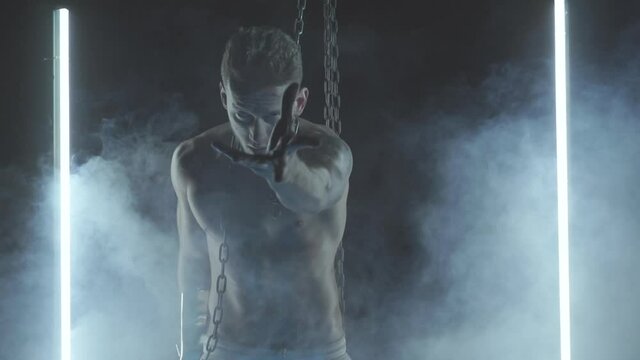 Sexy man dancing with chains in smoke