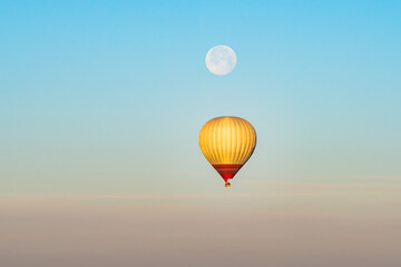 Hot air balloon flying over Cappadocia with full moon, pink sky