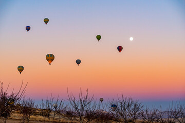 Hot air balloon flying over Cappadocia with full moon, pink sky