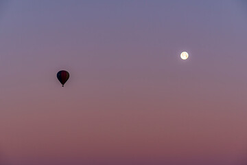 Hot air balloon flying over Cappadocia with full moon, pink sky