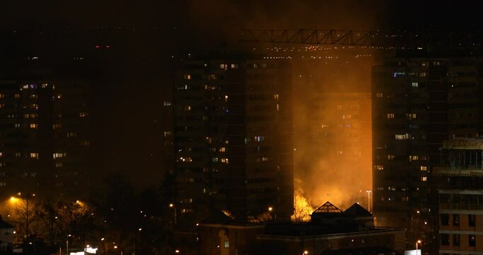 Fire in city at night, buildings and smoke lit by blazing flames, high angle shot