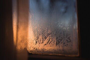 Looking beyond a curtain at shaped lines of frost on a window at a chilly sunrise