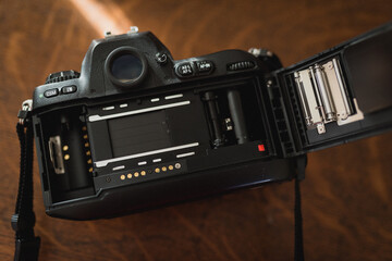 Fototapeta na wymiar Black film camera in upper left corner with back door open on a wooden background, closeup