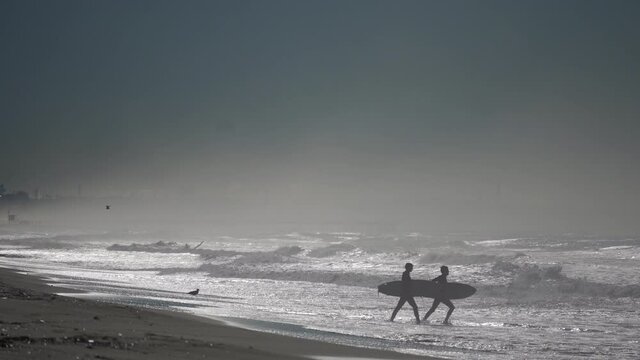 Surfers heading toward crashing waves on the shores of Southern California 