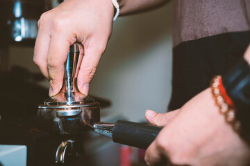 barista holding tamper in one hand going to press ground coffee in holder to make espresso