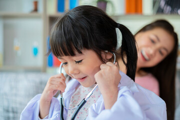 Cute little Asian girl act as nurse hold stethoscope listen to mom heart playing together at home, small Vietnamese child as doctor take care of mother or nanny, engaged in funny activity in bedroom - obrazy, fototapety, plakaty