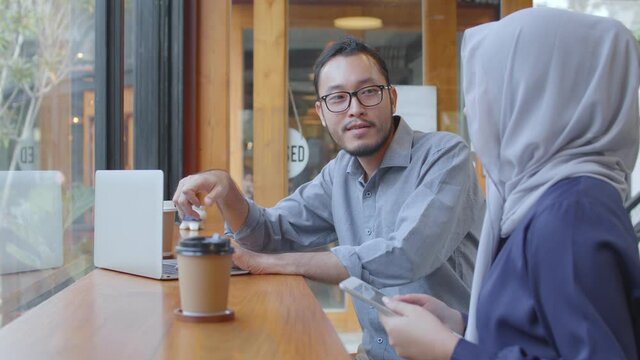 Happy diverse Asian Muslim young woman with friend chatting laughing at coffeehouse meeting, multicultural cheerful people group talking sit at caf&eacute; table drink coffee