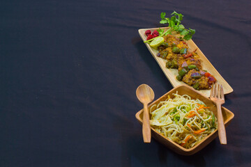 chilli chicken and noodles served on wooden plates with spoon and fork. delicious chinese food for copy space background.