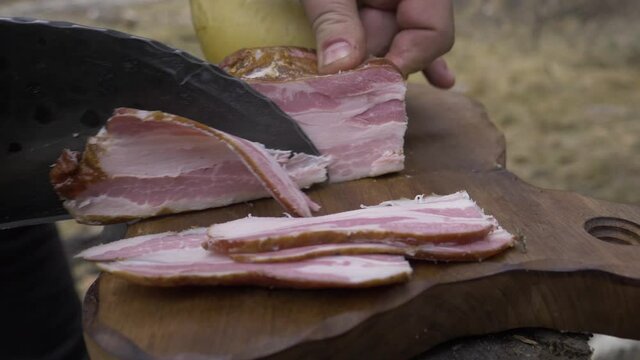 Traditional Satar knife cuts pork ham in nature, on an old oak chopper. The location is in the mountains for a winter time.