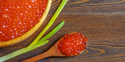 Red caviar in a wooden cup on a wooden background with a spoon.