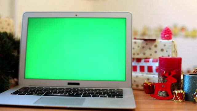 Green blank laptop screen with New Year presents on background. Winter holidays celebrating. Connect with friends. Chroma-key notebook. Free content. Mock up monitor. Online greeting. Internet surfing
