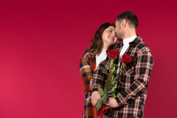 A loving couple with flowers on a red background look cute into each other's eyes. Empty side space.