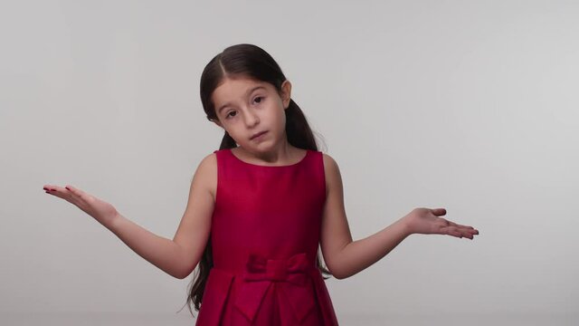 Surprised puzzled puzzled little girl in red dress posing in the studio isolated on white color background. His hands point to both sides.