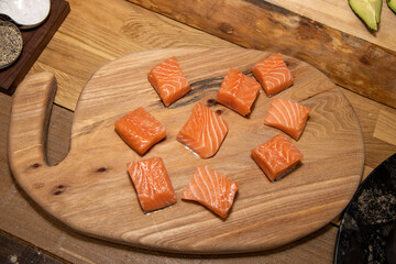 Diced sliced cubes of pink salmon fish on a wooden work top chopping board
