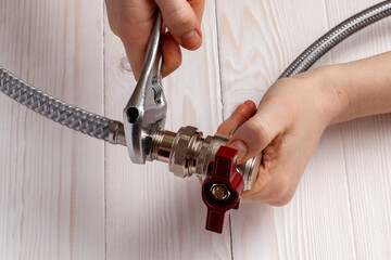 Female plumber connecting flexible hose to water ball valve. On white wooden background.