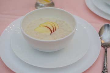 Oatmeal with apple for breakfast. Healthy eating. A useful breakfast. Porridge in a white ceramic cup on a pink tablecloth.